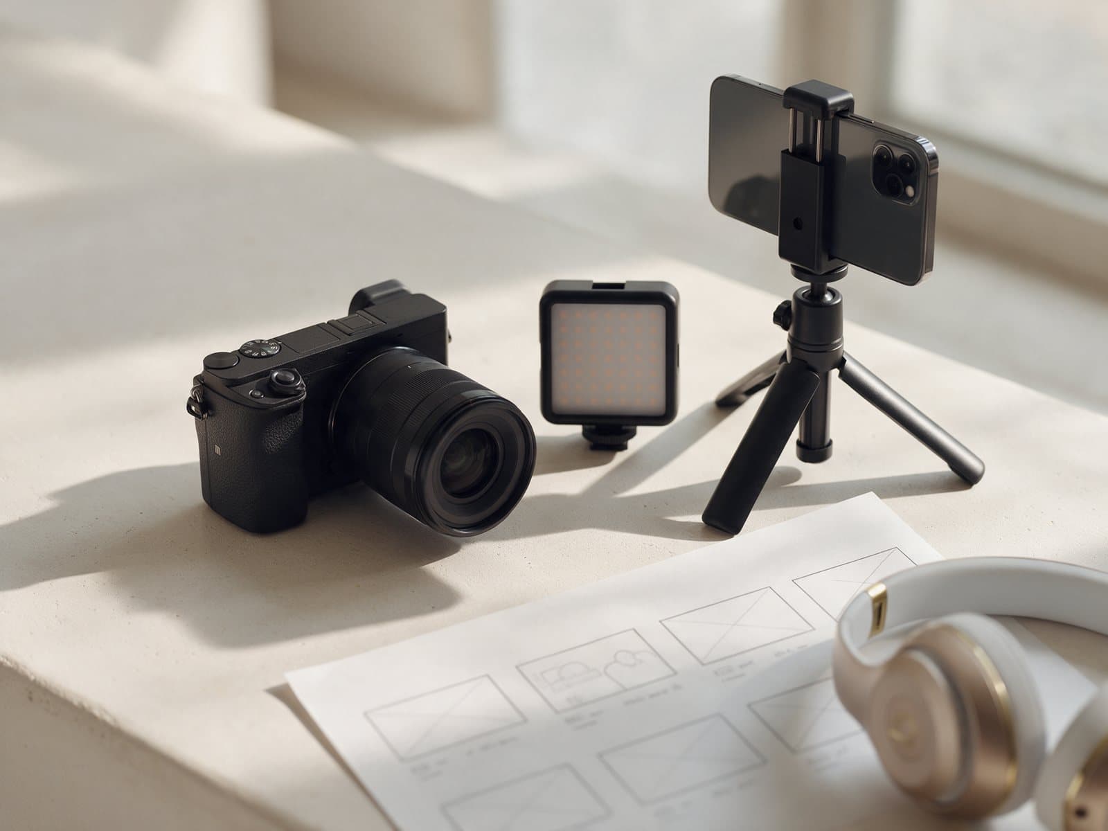Kamera, LED-Leuchte, Smartphone auf Stativ, Storyboard und Kopfhörer auf einem Steintisch